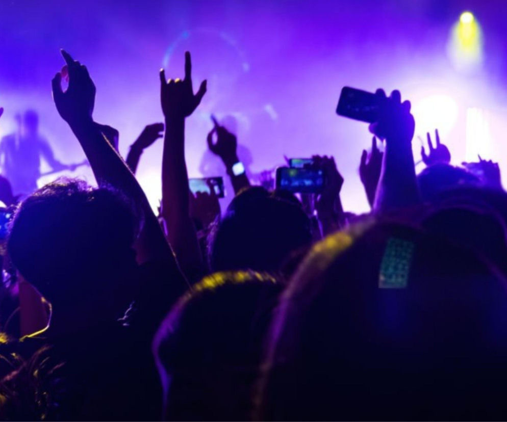 Tłum ludzi z rękami w górze na tle fioletowych świateł estrady. O BitterSweet Festival w Poznaniu przeczytasz w Eskice.