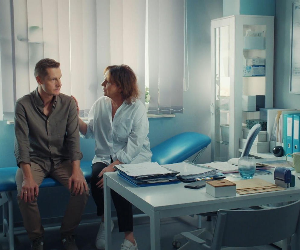 Paweł Zduński siedzi na kozetce, a obok niego Marysia Rogowska, która kładzie mu dłoń na ramieniu, pocieszając go. Scena rozgrywa się w gabinecie lekarskim, gdzie Paweł dzieli się z matką trudnymi informacjami o chorobie Franki. Więcej na Super Seriale.