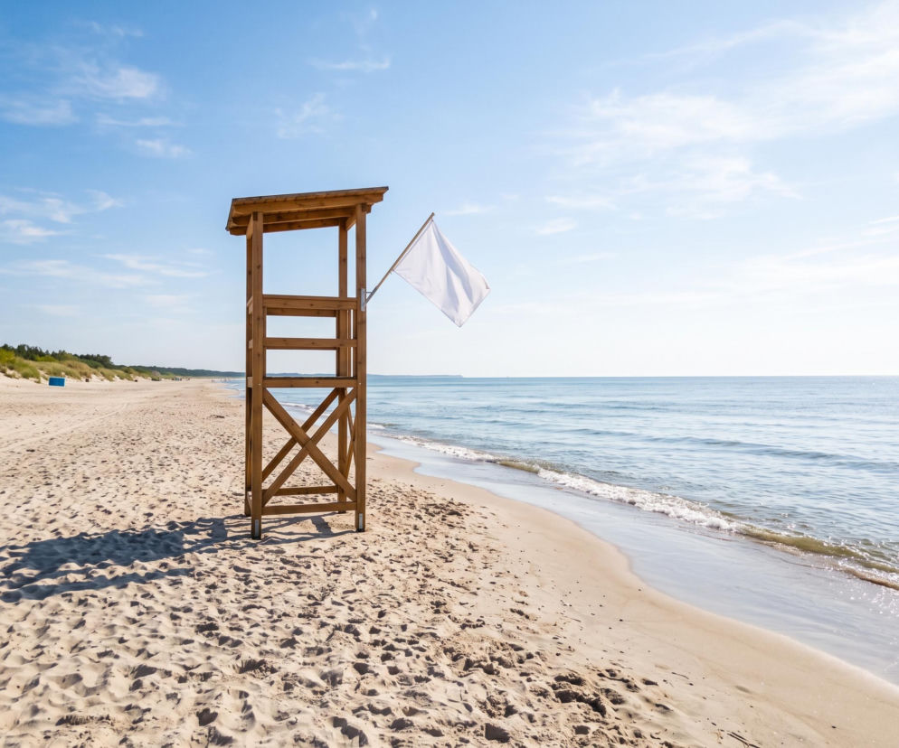 Drewniana wieża ratownicza z białą flagą na pustej plaży. O bezpiecznej kąpieli w Dźwirzynie przeczytasz na SE Szczecin.
