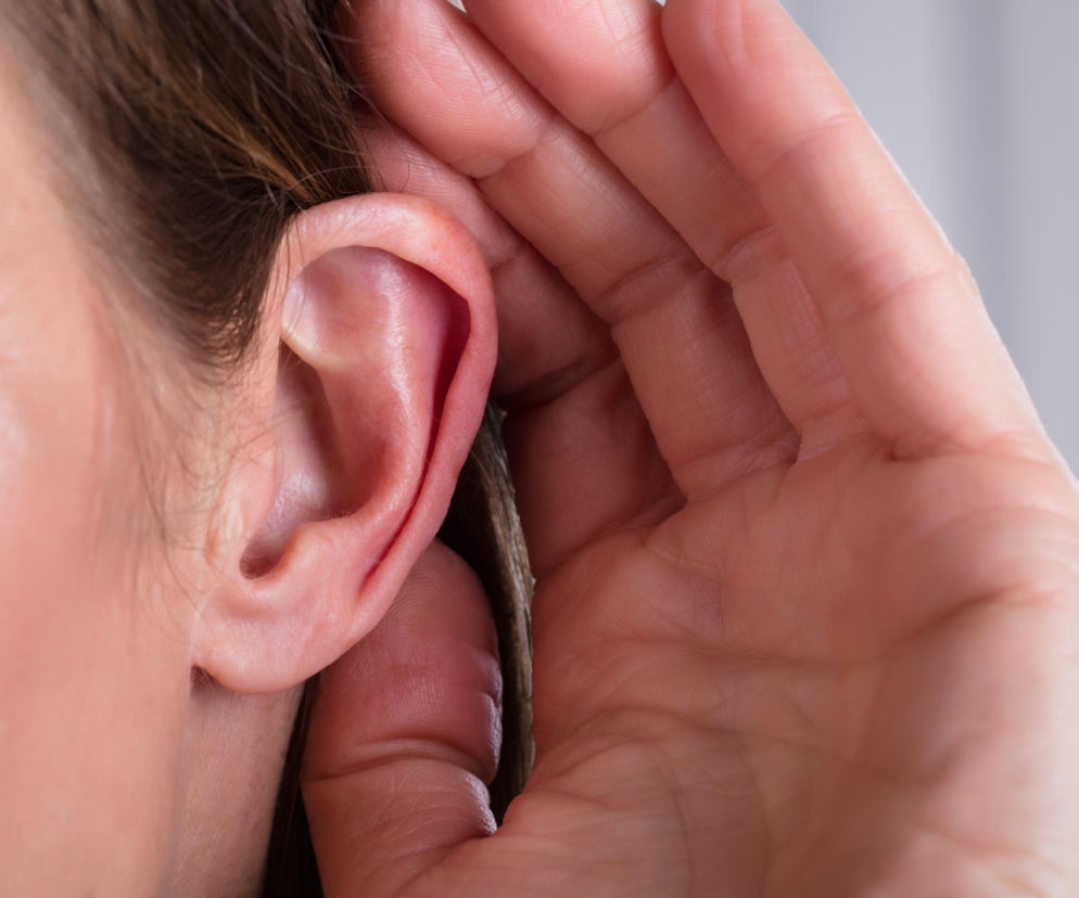 Ucho kobiety, której dłoń dotyka małżowiny usznej, symbolizuje nasłuchiwanie i problemy ze słuchem, zwłaszcza ukryty niedosłuch. Więcej o subtelnych sygnałach niedosłuchu na Poradnik Zdrowie.