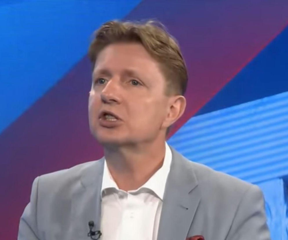 Dr Artur Bartoszewicz, ekonomista i komentator polityczny, podczas wywiadu. Mężczyzna w jasnej marynarce i białej koszuli, z krótkimi, jasnymi włosami, mówi z otwartymi ustami, wyrażając swoje zdanie na temat patologii w polskiej służbie zdrowia, o czym przeczytasz na naszym portalu.