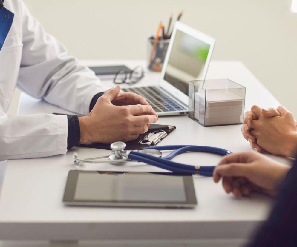 Lekarz rozmawiający z parą pacjentów przy biurku. O rządowym programie in vitro w klinice INVICTA przeczytasz na Eska.