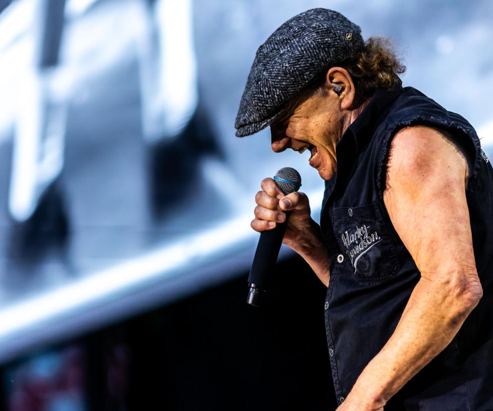 Brian Johnson z AC/DC śpiewa do mikrofonu podczas koncertu. O historii wokalisty przeczytasz na EskaRock.