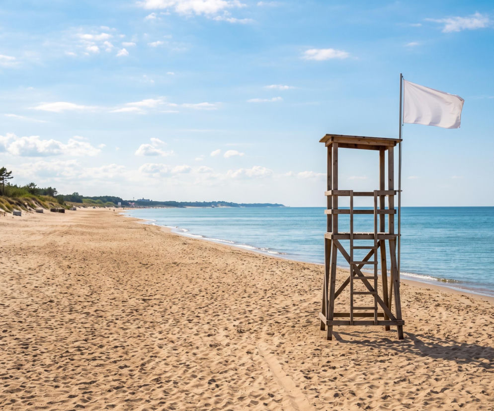 Drewniana wieża ratownicza z białą flagą na pustej, piaszczystej plaży w Mielnie. O warunkach kąpieli pisze SE Szczecin.