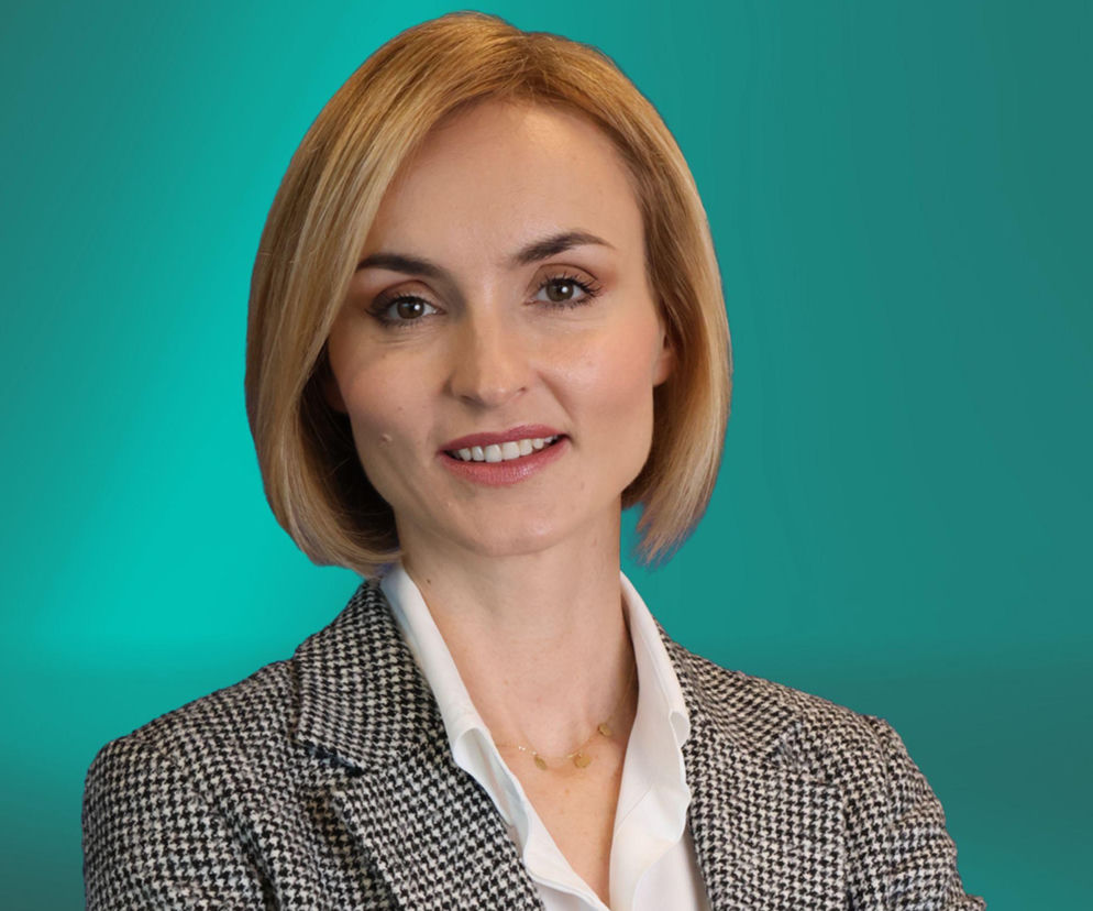 Portret uśmiechniętej kobiety w marynarce na zielonym tle. O zagranicznych inwestycjach w Polsce przeczytasz na Eska.