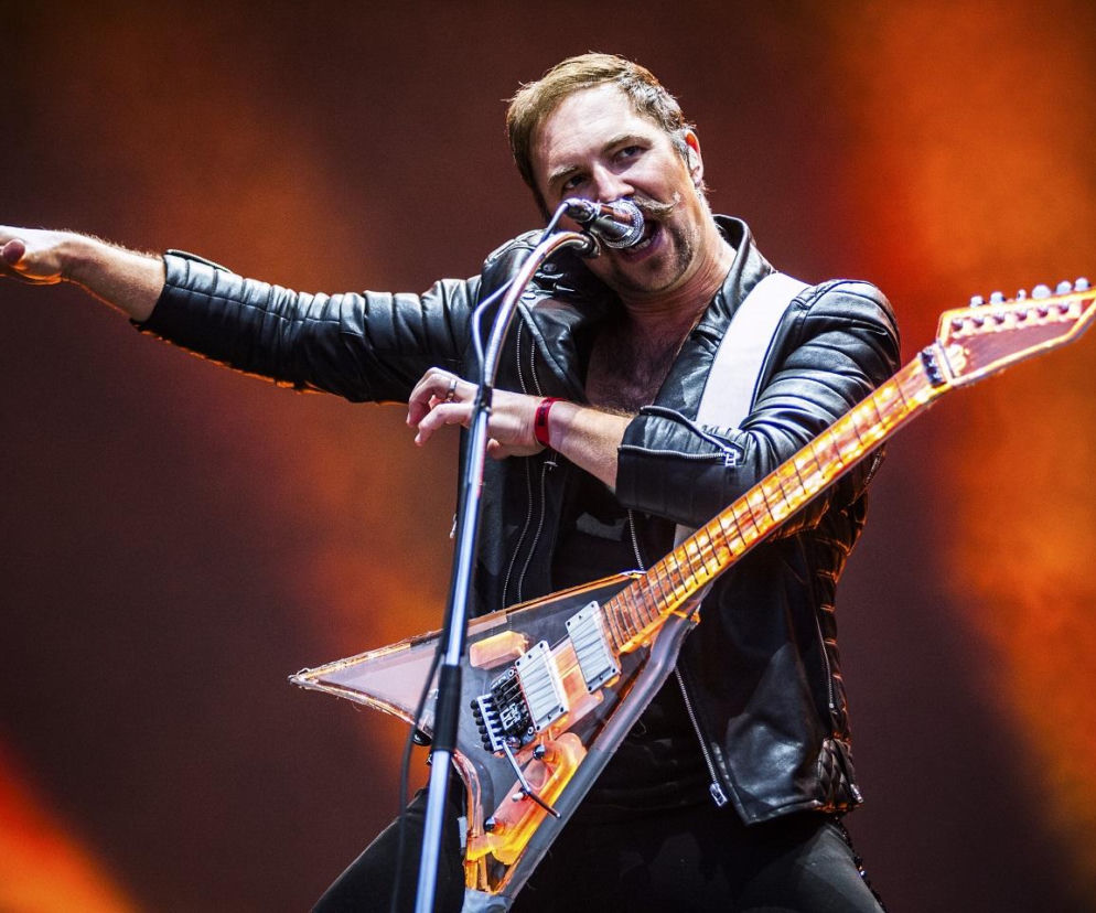 Muzyk w skórzanej kurtce śpiewa i gra na gitarze elektrycznej podczas koncertu. O Rockowizna Festiwal czytaj na EskaRock.