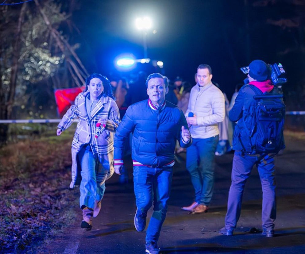 Lucynka i Maurycy biegną ulicą, z wyraźnym przerażeniem na twarzach, w tle widać ekipę filmową oraz światła policyjnego radiowozu, co sugeruje tragiczny wypadek autokaru z ich córką, co jest zapowiedzią emocjonującego odcinka serialu Pierwsza miłość na Super Seriale.