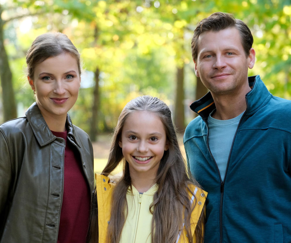 Uśmiechnięta Natalka (Dominika Suchecka) w skórzanej kurtce, uśmiechnięty Adam (Patryk Szwichtenberg) w turkusowej bluzie i zadowolona Hania (Wiktoria Basik) w żółtej kamizelce na tle zieleni, cała trójka pozuje do zdjęcia. Więcej o tym, co się wydarzy, przeczytasz na Super Seriale.