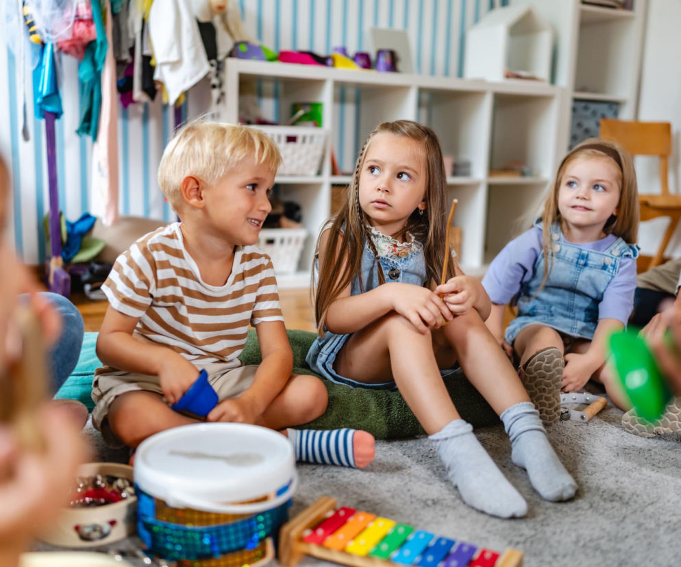 Dzieci siedzą na podłodze z instrumentami. Dziewczynka w środku patrzy z powagą. O perfekcjonizmie u dzieci czytaj w SE.
