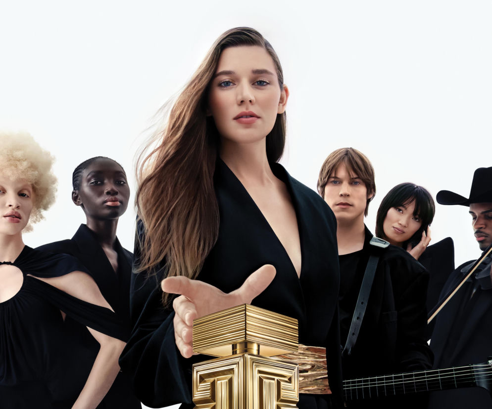 Kobieta w czarnej kreacji obok złocistego flakonu perfum Destin de Balmain. O nowościach w SE przeczytasz w artykule.