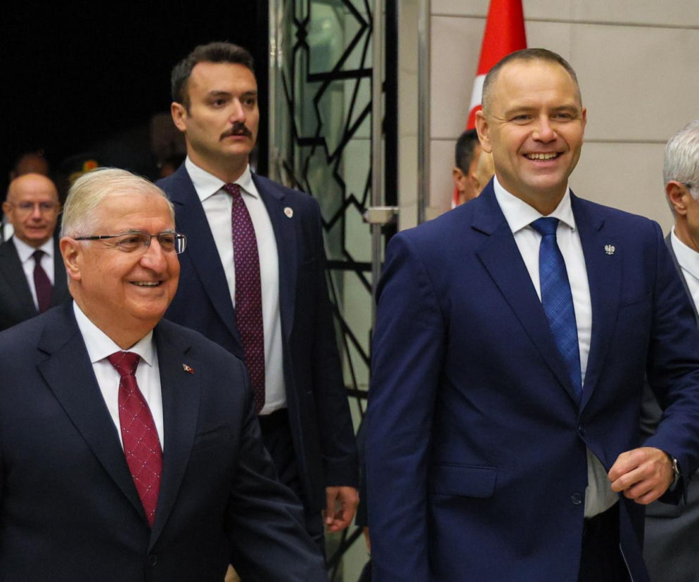 Prezydent Karol Nawrocki (po prawej) z uśmiechem idzie obok tureckiego urzędnika w okularach, podczas wizyty w Turcji. Za nimi, z wąsami, widoczny ochroniarz. O szczegółach wizyty i spotkań, przeczytasz na naszym portalu.