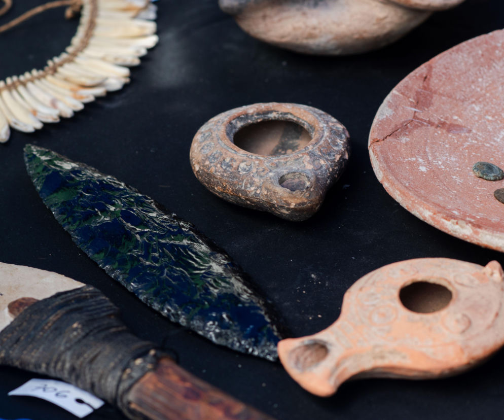 Starożytne narzędzia z brązu, ceramika i monety na ciemnym tle. O odkryciach archeologów z Polski przeczytasz w Eska.
