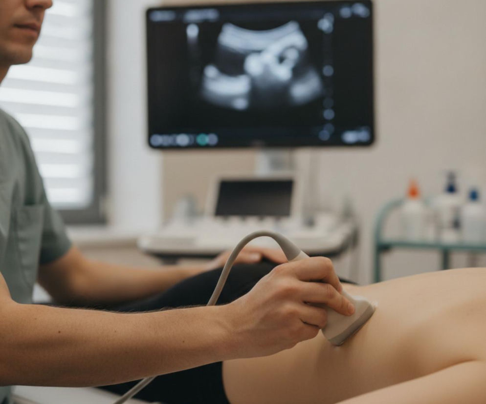 Lekarz wykonujący badanie ultrasonograficzne pleców pacjenta, z monitorem USG w tle, na którym widoczne są obrazy wewnętrzne. To badanie pomaga w diagnostyce fibromialgii, o której można przeczytać na portalu Poradnik Zdrowie.