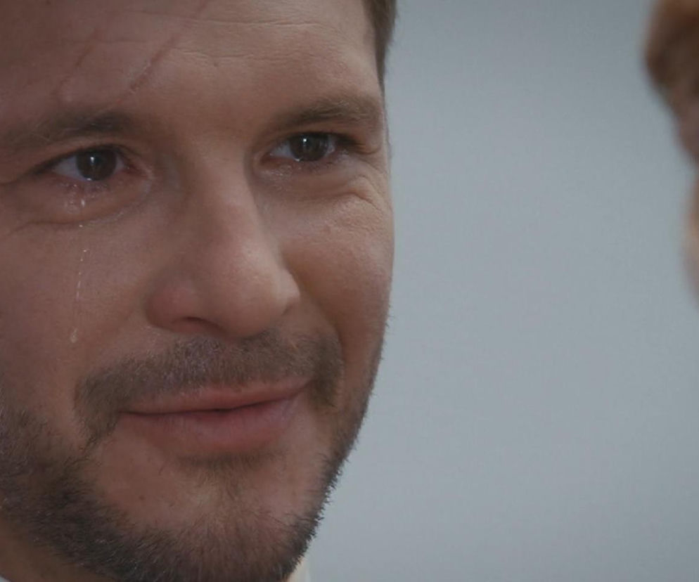 Zbliżenie na zapłakaną twarz Marcina Chodakowskiego (Mikołaj Roznerski) podczas ślubu z Kamą (Michalina Sosna) w serialu M jak miłość, ze łzą spływającą po policzku. Emocje bohatera widać na jego twarzy, co znajdziesz w artykułach na Super Seriale.