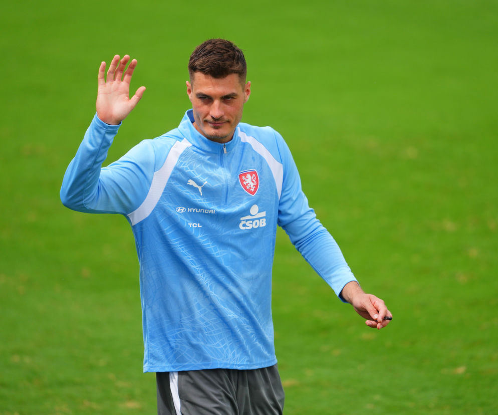 Piłkarz Patrik Schick w niebieskiej koszulce reprezentacji Czech, z numerem na piersi, podnosi dłoń, machając na tle zielonej murawy, symbolizując pożegnanie z kadrą. O jego decyzji o rezygnacji z gry w reprezentacji Czech po klęsce na MŚ 2026 przeczytasz więcej na naszym portalu.
