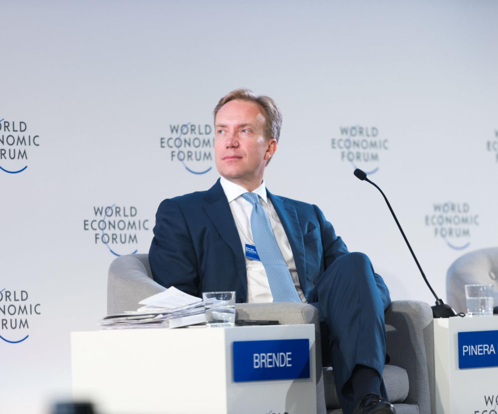 Boerge Brende, ubrany w granatowy garnitur i krawat, siedzi na krześle konferencyjnym, przed nim widoczna jest tabliczka z jego nazwiskiem. W tle logo Światowego Forum Ekonomicznego. Więcej o rezygnacji Brendego przeczytasz na Super Biznes.
