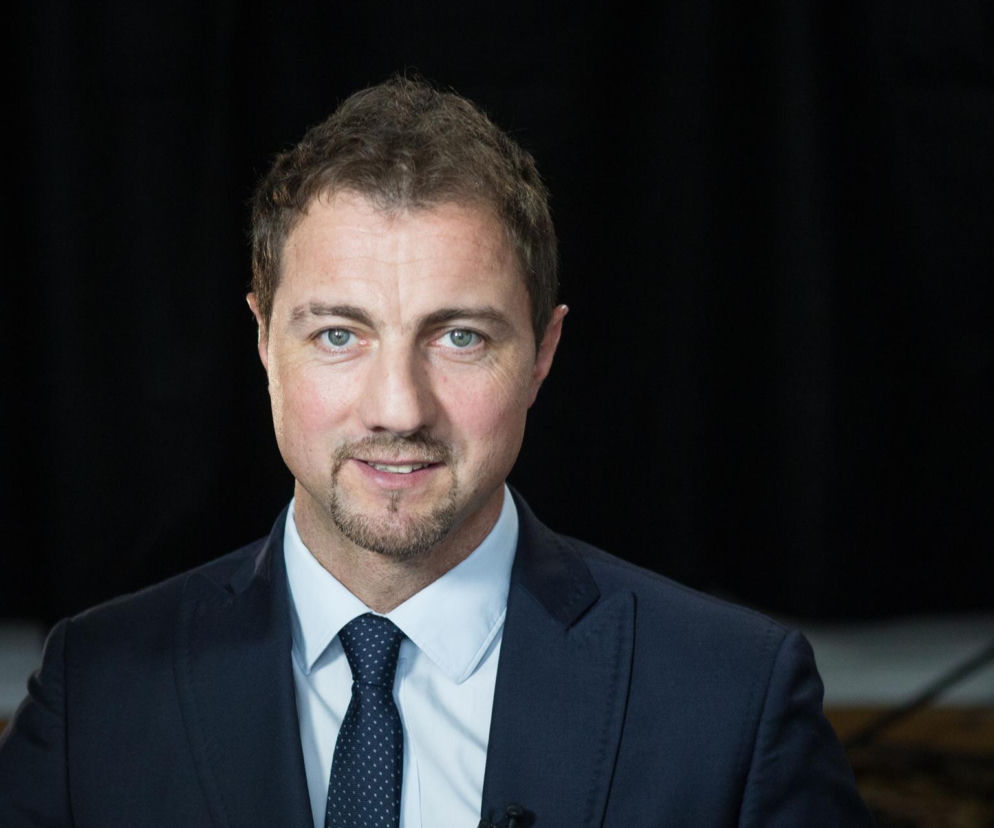 Były bramkarz Jerzy Dudek w granatowej marynarce, białej koszuli i krawacie w kropki, z delikatnym zarostem i uśmiechem, patrzący prosto w obiektyw. Całość na ciemnym, rozmytym tle. Więcej na ten temat przeczytasz na naszym portalu.
