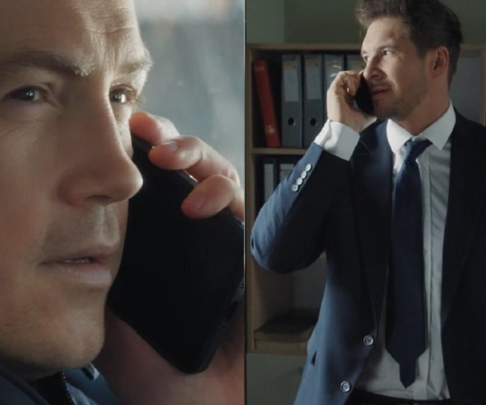 Mężczyzna w niebieskiej marynarce rozmawia przez telefon, patrząc z zamyśleniem. Obok niego, drugi mężczyzna w garniturze również prowadzi rozmowę telefoniczną, stojąc w biurze. Marcin i Jakub w nowej pracy w „M jak miłość”. Obejrzyj te i inne Super Seriale.