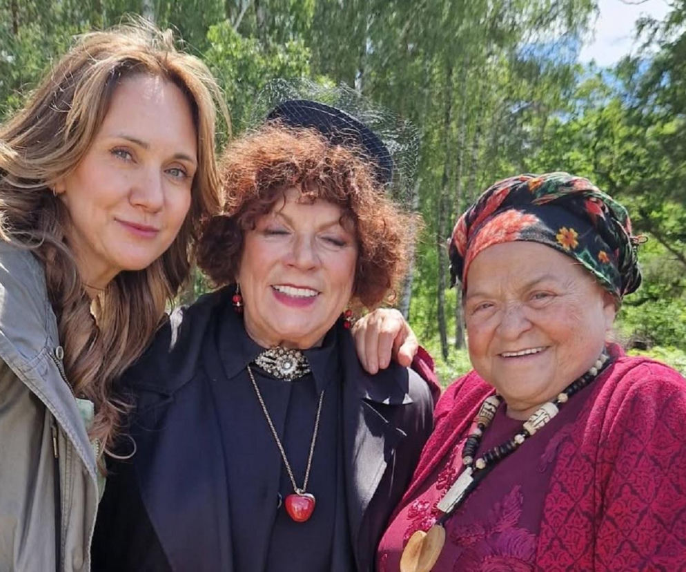 Ilustracja trzech uśmiechniętych aktorek: Ilona Ostrowska (Lucy), Elżbieta Romanowska (wiedźma) i Grażyna Zielińska (babka) z serialu Ranczo, stojących obok siebie na tle zielonego lasu. To zdjęcie z planu serialu zapowiada nowy sezon Rancza na Super Seriale.