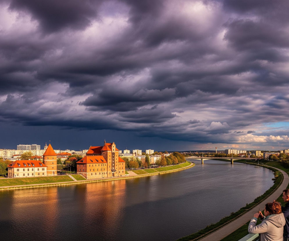 Pochmurne niebo z ciemnymi, burzowymi chmurami dominują nad sceną, z jaśniejszym, błękitnym niebem i białymi obłokami widocznymi w prawym górnym rogu. Poniżej rozciąga się rzeka, odbijająca ciemne barwy nieba, z rzędem zabytkowych budynków o pomarańczowych dachach po jej lewej stronie, z których jeden wyróżnia się wieżą. Brzeg rzeki porośnięty jest zieloną trawą i drzewami o jesiennych barwach, za którymi wznoszą się liczne budynki miejskie, w tym wieżowce. W oddali po prawej widoczny jest most, a na pierwszym planie, po prawej stronie kadru, grupka ludzi stoi na moście lub platformie widokowej, opierając się o zieloną barierkę i obserwując panoramę.