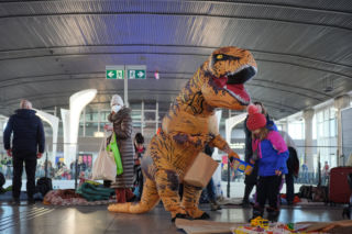 Dinozaur na Dworcu Centralnym - mieszkaniec Warszawy wywołuje uśmiech na twarzach małych uchodźców