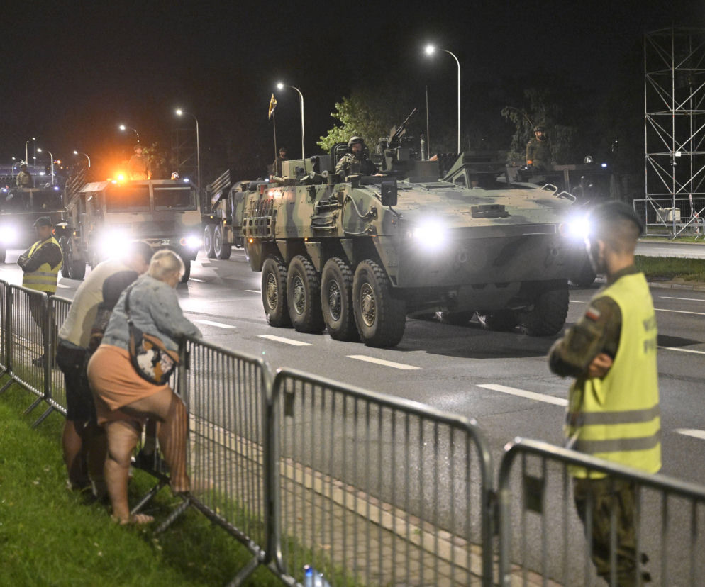 Pojazdy wojskowe na Wisłostradzie nocą obserwowane przez ludzi za barierami. O próbie defilady przeczytasz w Eska Warszawa.