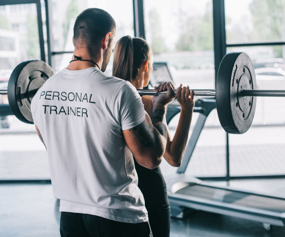 Trener personalny pomaga sportsmence wykonywać ćwiczenia ze sztangą na siłowni. 