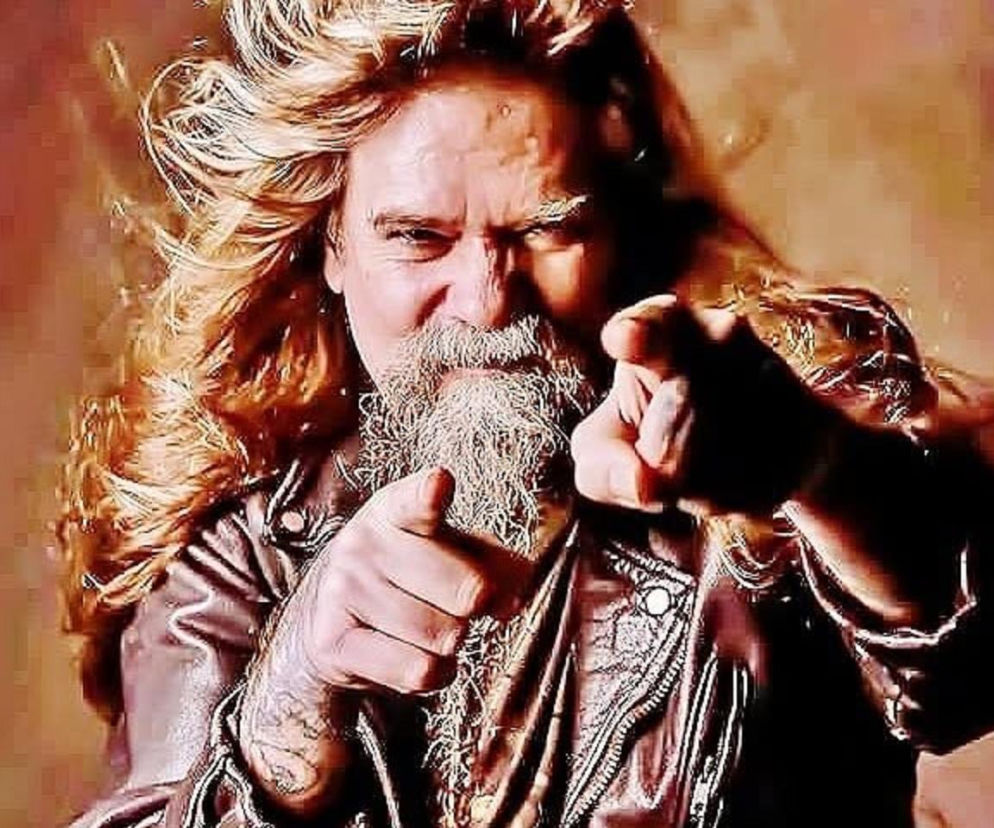Gitarzysta Chris Holmes celuje palcami przed siebie. O zbiórce na leczenie muzyka przeczytasz na EskaRock.
