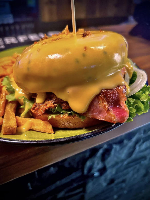 Burger z autorską, szarpaną wieprzowiną oblany sosem serowym w zestawie z frytkami