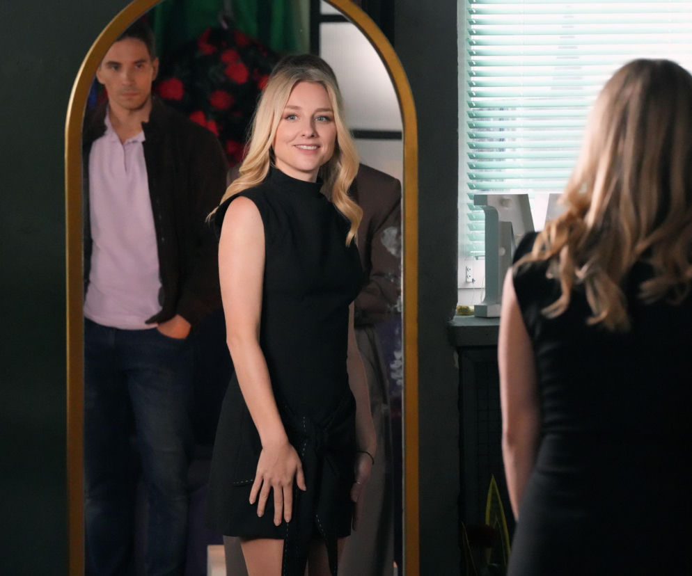 Młoda kobieta w czarnej sukience uśmiecha się, przeglądając w lustrze, za nią w odbiciu widać mężczyznę. Scena nawiązuje do serialu Barwy szczęścia, gdzie Grażyna rozkwita przy Patryku, co wzbudza zazdrość Tomka. Więcej o ich relacjach przeczytasz na Super Seriale.