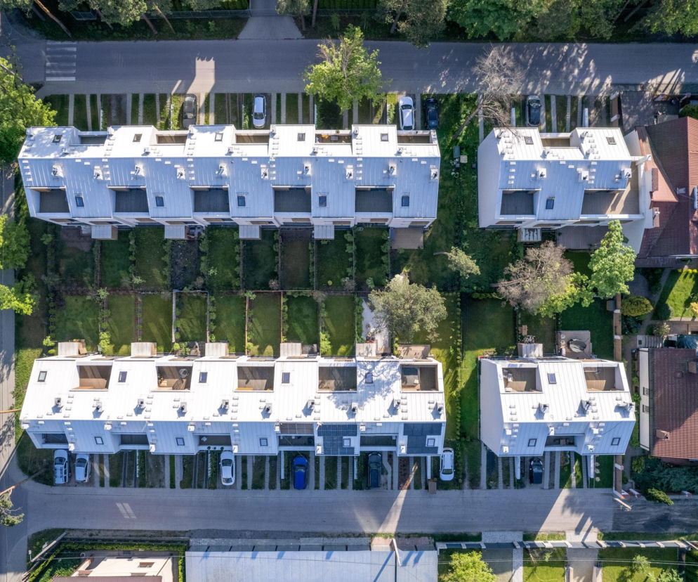 Osiedle Leśna w Otwocku, minimalistyczne bryły z białymi elewacjami i dwuspadowymi dachami, widoczne z lotu ptaka. Projekt 77 Studio architektury z dbałością o detal nawiązujący do świdermajerów, z otwartą przestrzenią bez ogrodzeń. Więcej o tym na Architektura Murator Plus.