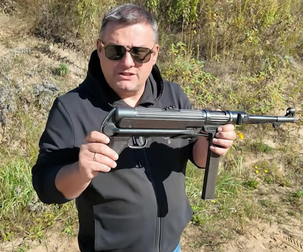 Mężczyzna trzyma pistolet maszynowy MP 38 na tle traw. O historii tej rzadkiej broni przeczytasz na SE Portal Obronny.