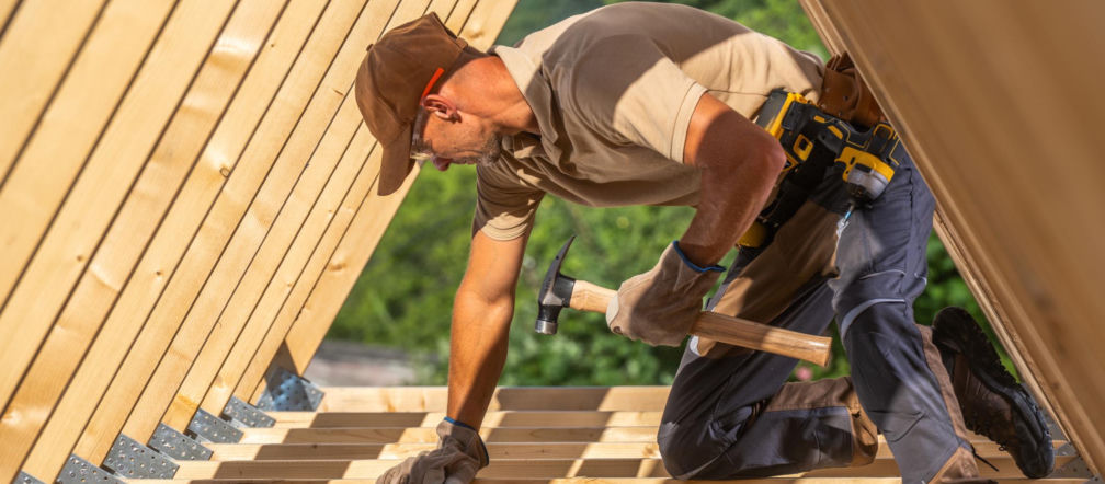 Pracownik budowlany na dachu w trakcie prac ciesielskich.