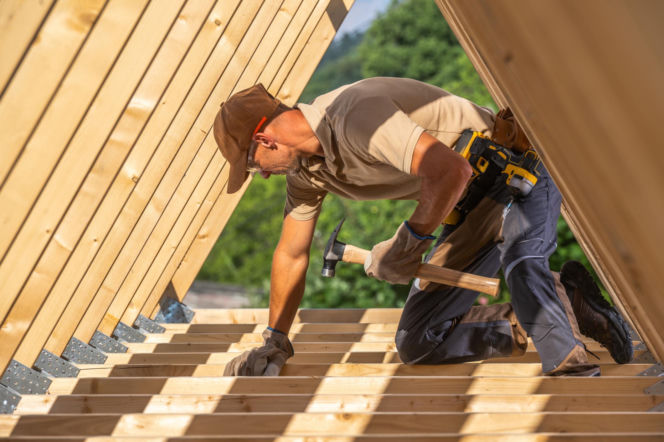 Pracownik budowlany na dachu w trakcie prac ciesielskich.