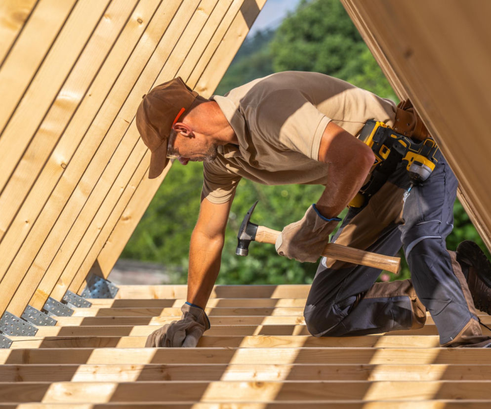 Pracownik budowlany na dachu w trakcie prac ciesielskich.