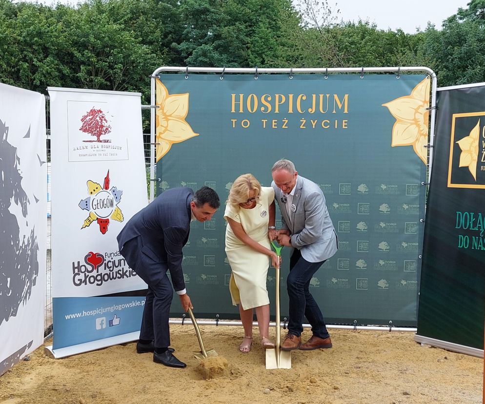 Trzy osoby wbijają złote łopaty w piasek przed banerem z napisem Hospicjum. O inwestycji przeczytasz na Radioplus.