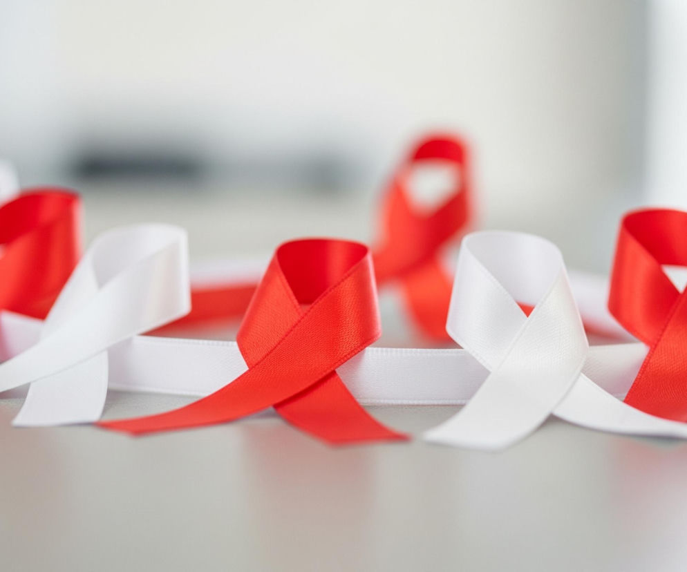 Szereg zawiniętych wstążek, ułożonych naprzemiennie w kolorach czerwonym i białym, rozciąga się w poprzek kadru. Wstążki te tworzą pętle i krzyżują się ze sobą, leżąc na jasnej, szarej powierzchni. Obiekty znajdujące się z tyłu są rozmyte, co wskazuje na płytką głębię ostrości.