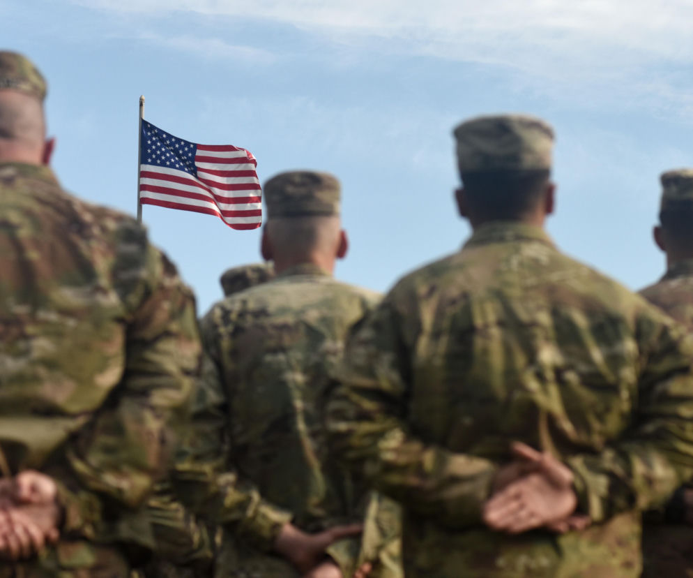 Żołnierze w mundurach moro patrzą na flagę USA. O planach budowy bazy wojskowej w Szczecinie przeczytasz na SE Szczecin.