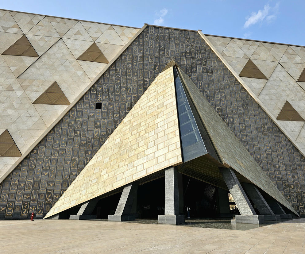 Fasada Wielkiego Muzeum Egipskiego z wejściem w kształcie piramidy i ścianami pokrytymi hieroglifami, symbolizująca bogatą kulturę i architekturę starożytnego Egiptu. Więcej o tym na portalu Architektura Murator Plus.