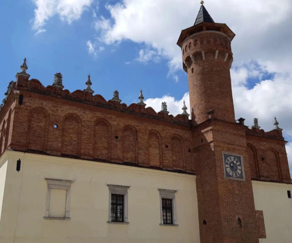 Budynek Urzędu Miasta w Tarnowie z charakterystyczną czerwoną cegłą, renesansowymi attykami i wieżą zegarową, na tle błękitnego nieba z białymi chmurami. O Budżecie Obywatelskim Tarnowa i innych ważnych dla miasta sprawach przeczytasz na naszym portalu.