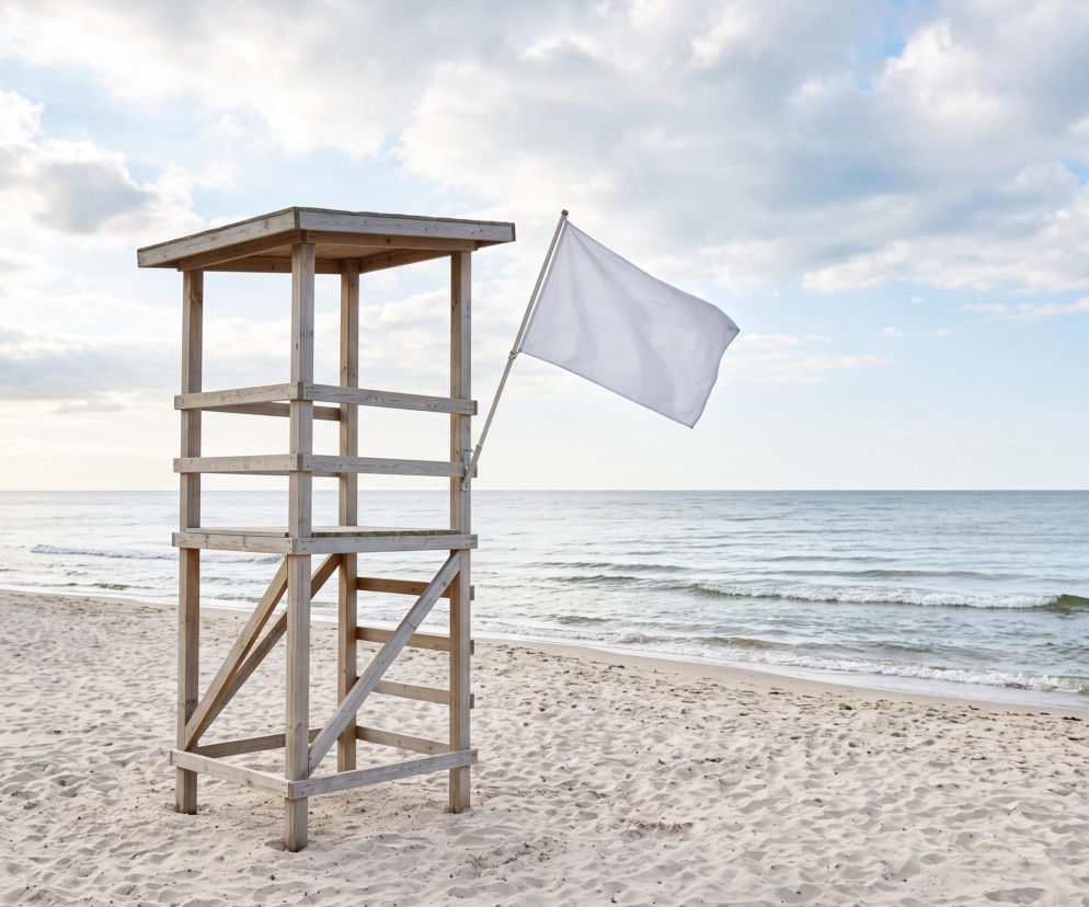 Drewniana wieża ratownika na piaszczystej plaży z białą flagą. O bezpieczeństwie w Międzyzdrojach przeczytasz na SE Szczecin.
