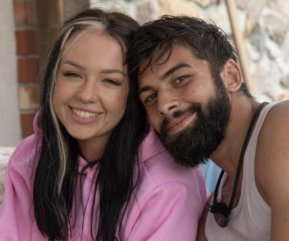 Paulina i Aksel, uczestnicy programu Farma, uśmiechający się i tulący do siebie, Paulina w różowej bluzie z kapturem, a Aksel w białym podkoszulku. Para, której relacja wzbudza emocje fanów, spekulujących, czy są razem po programie. Więcej o ich losach na Super Seriale.