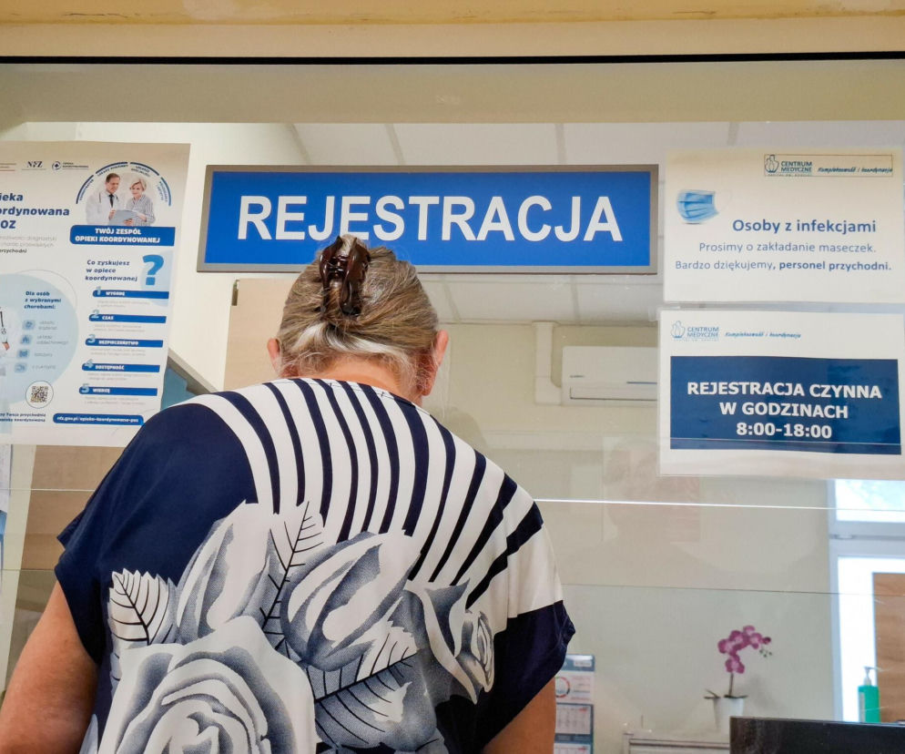 Kobieta stoi przy okienku z napisem Rejestracja. O przywilejach dla pacjentów na NFZ przeczytasz na Eska.