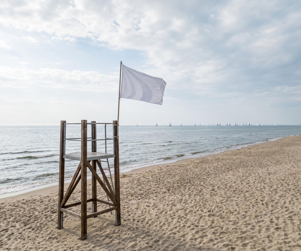 Wieża ratownicza z białą flagą na plaży w Dziwnowie. W tle żaglówki. O braku sinic przeczytasz na SE Szczecin.