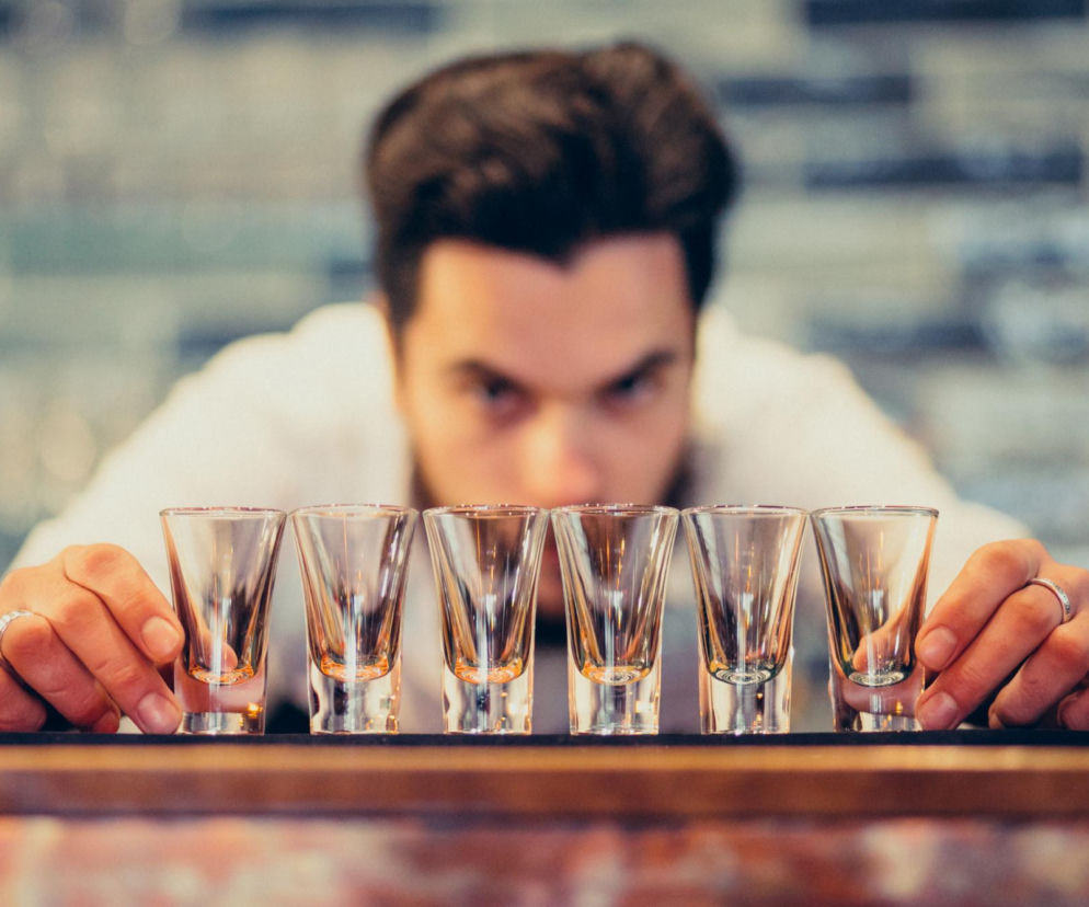 Mężczyzna ustawia w rzędzie sześć pustych kieliszków do alkoholu. O planowanych podwyżkach akcyzy przeczytasz na Eska.