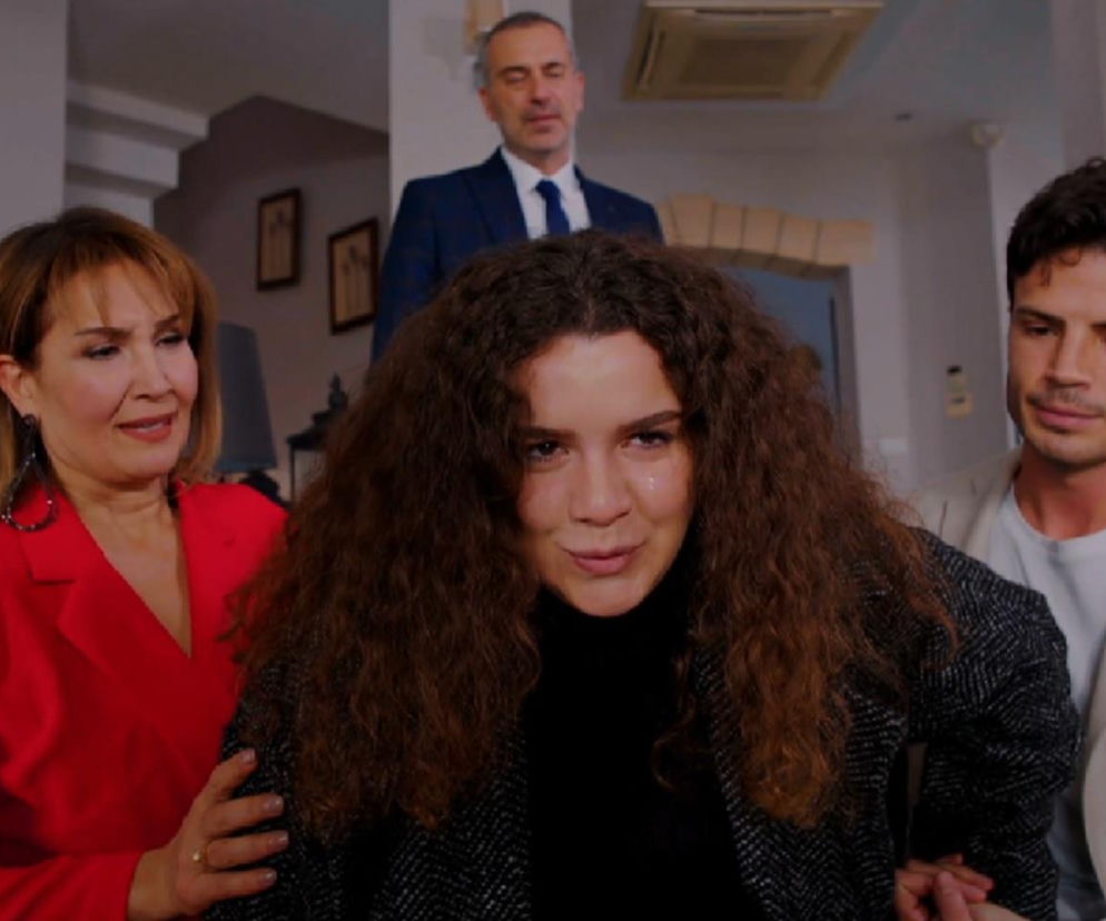 Melis z kręconymi włosami udająca skurcze, trzymana przez Feraye w czerwonej marynarce i Egego w beżowej marynarce. W tle Bulent w garniturze. Scena z serialu Miłość i nadzieja o aktorskim popisie Melis i wyrzutach sumienia Egego. Więcej na Super Seriale.