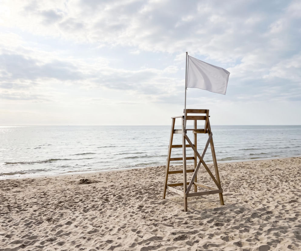Drewniana wieżyczka ratownicza z białą flagą na pustej plaży w Międzyzdrojach. O bezpieczeństwie w wodzie czytaj w SE Szczecin.
