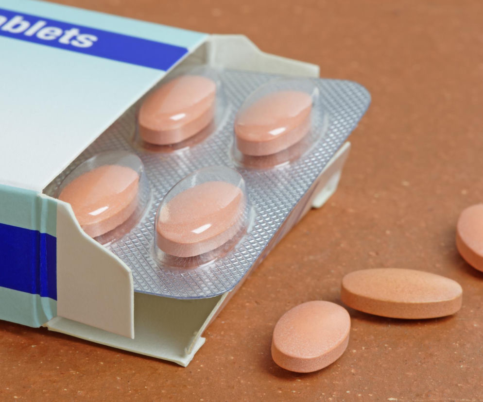 Pudełko z lekiem zawierające blister ze statynami na obniżenie cholesterolu oraz trzy tabletki luzem na brązowej powierzchni. Na portalu Poradnik Zdrowie znajdziesz artykuł o skutkach ubocznych statyn.