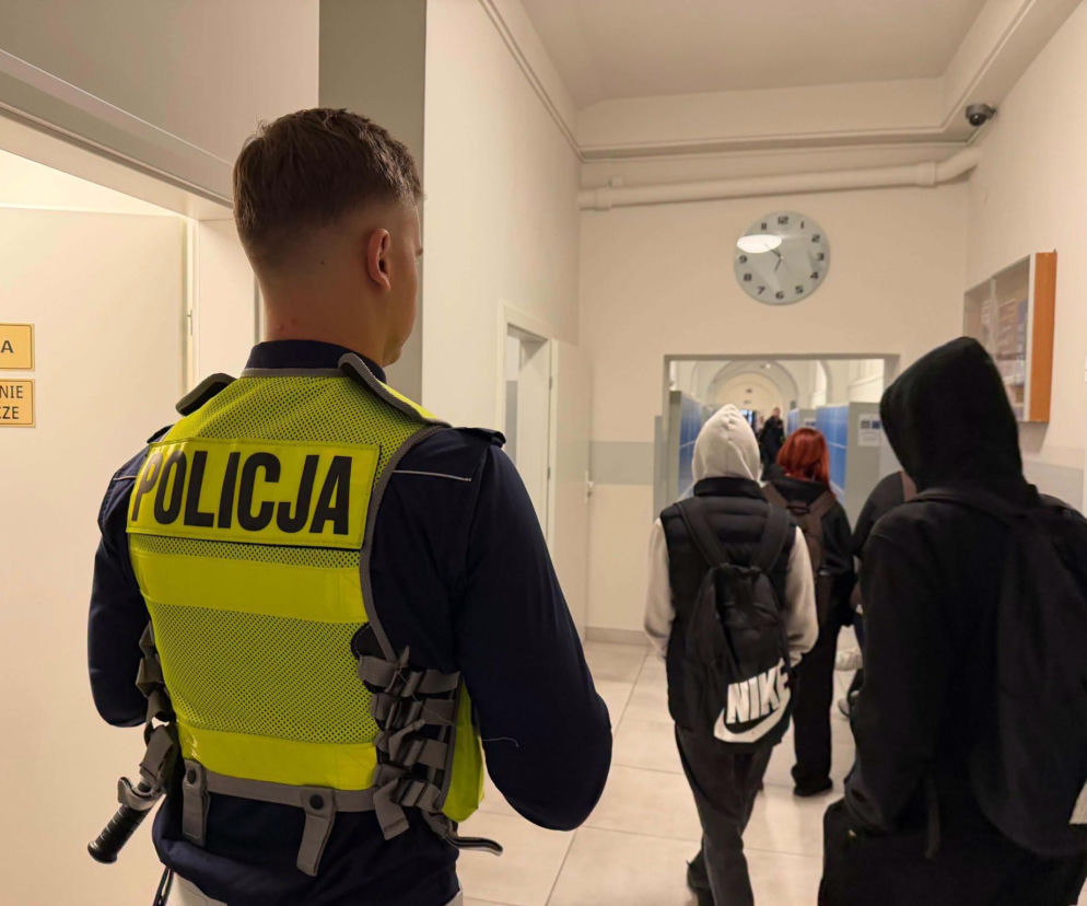 Policjant w odblaskowej kamizelce pilnuje bezpieczeństwa uczniów na szkolnym korytarzu. O patrolach pisze Eska Białystok.