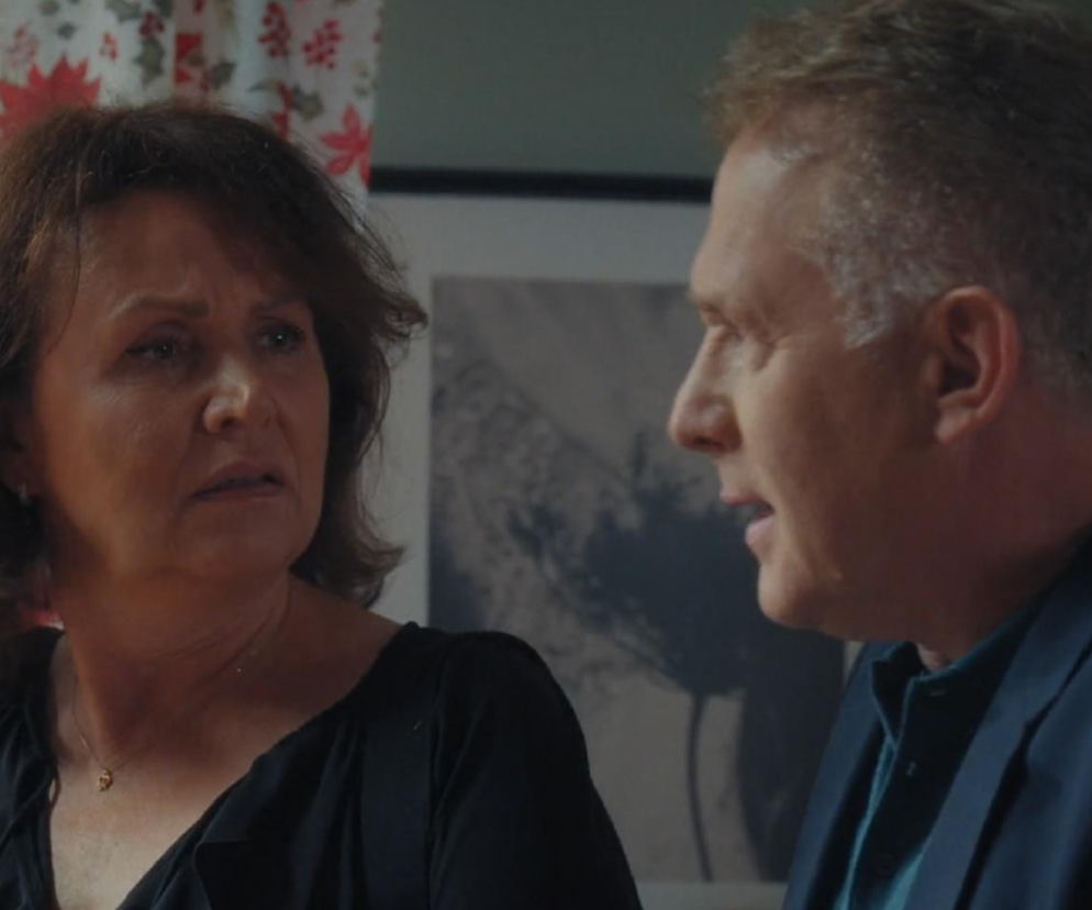 Marysia (Małgorzata Pieńkowska) z zatroskaną miną patrzy na Artura (Robert Moskwa), który w ciemnoniebieskiej marynarce rozmawia z nią, odwrócony profilem. Scena z serialu M jak miłość zapowiada kryzys w ich małżeństwie, o czym więcej można przeczytać na portalu Super Seriale.